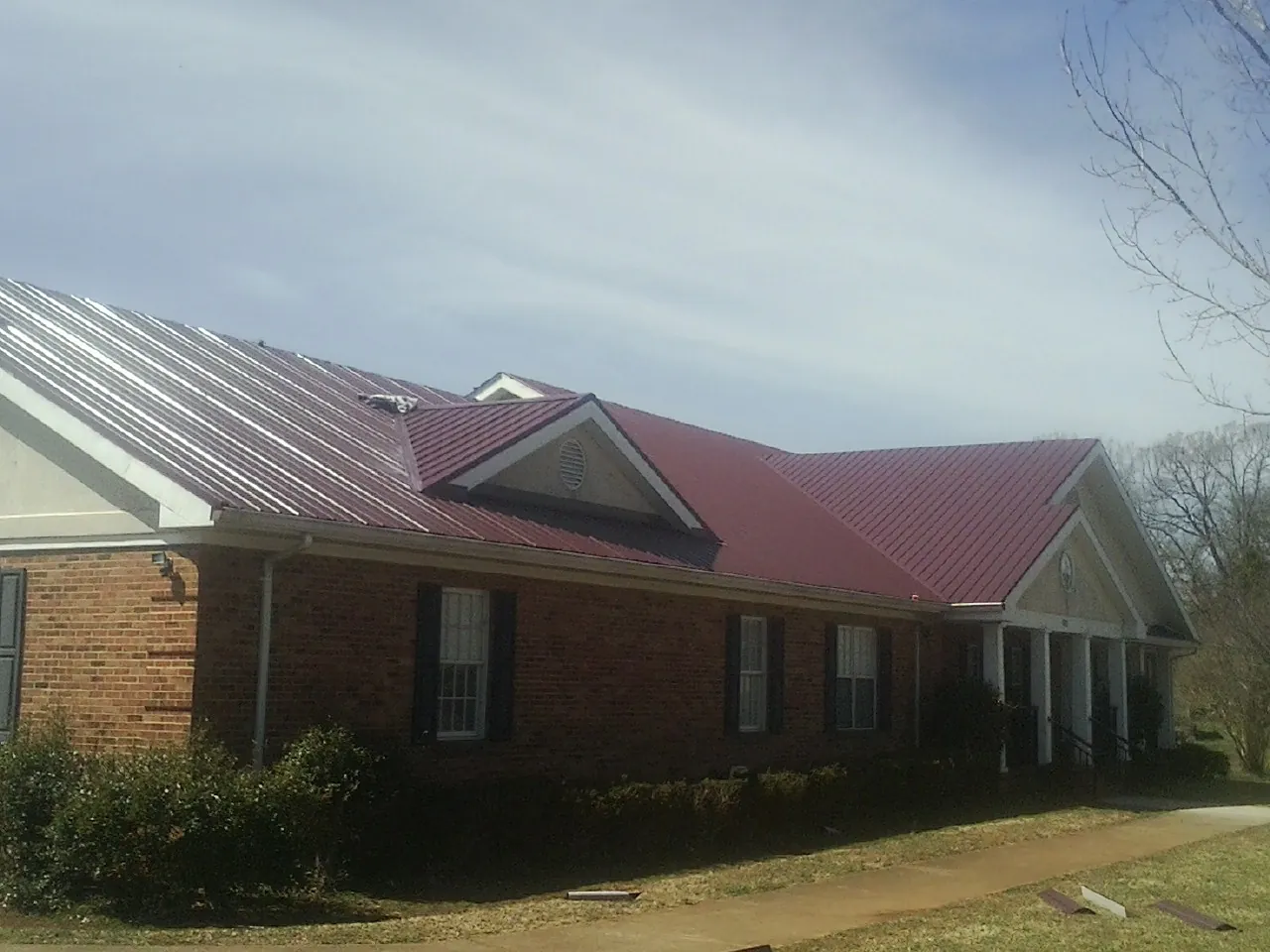 Red metal roof with gabled entries on a long brick building, from a Hail Damage Roof Repair job in Plain Dealing