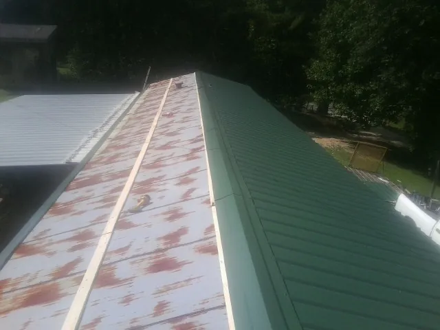 Old rusted panels beside newly installed green metal roofing — Wind Damage Roof Repair by Roofing Brothers in Plain Dealing
