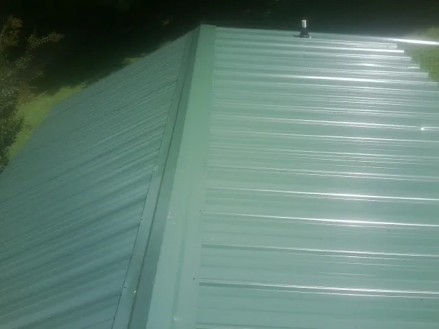 New green metal panels meeting at the ridge of a roof — Flat Roof Repair work by our crew in Plain Dealing