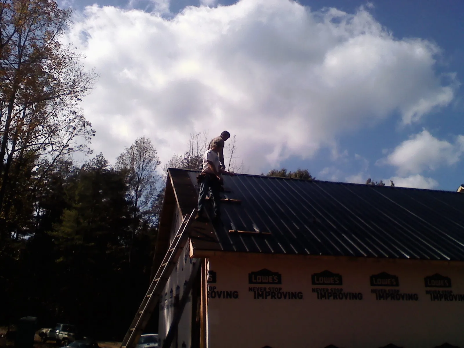 Roofer fastening dark metal panels high against a cloudy sky, from a Roof Inspection job in Plain Dealing