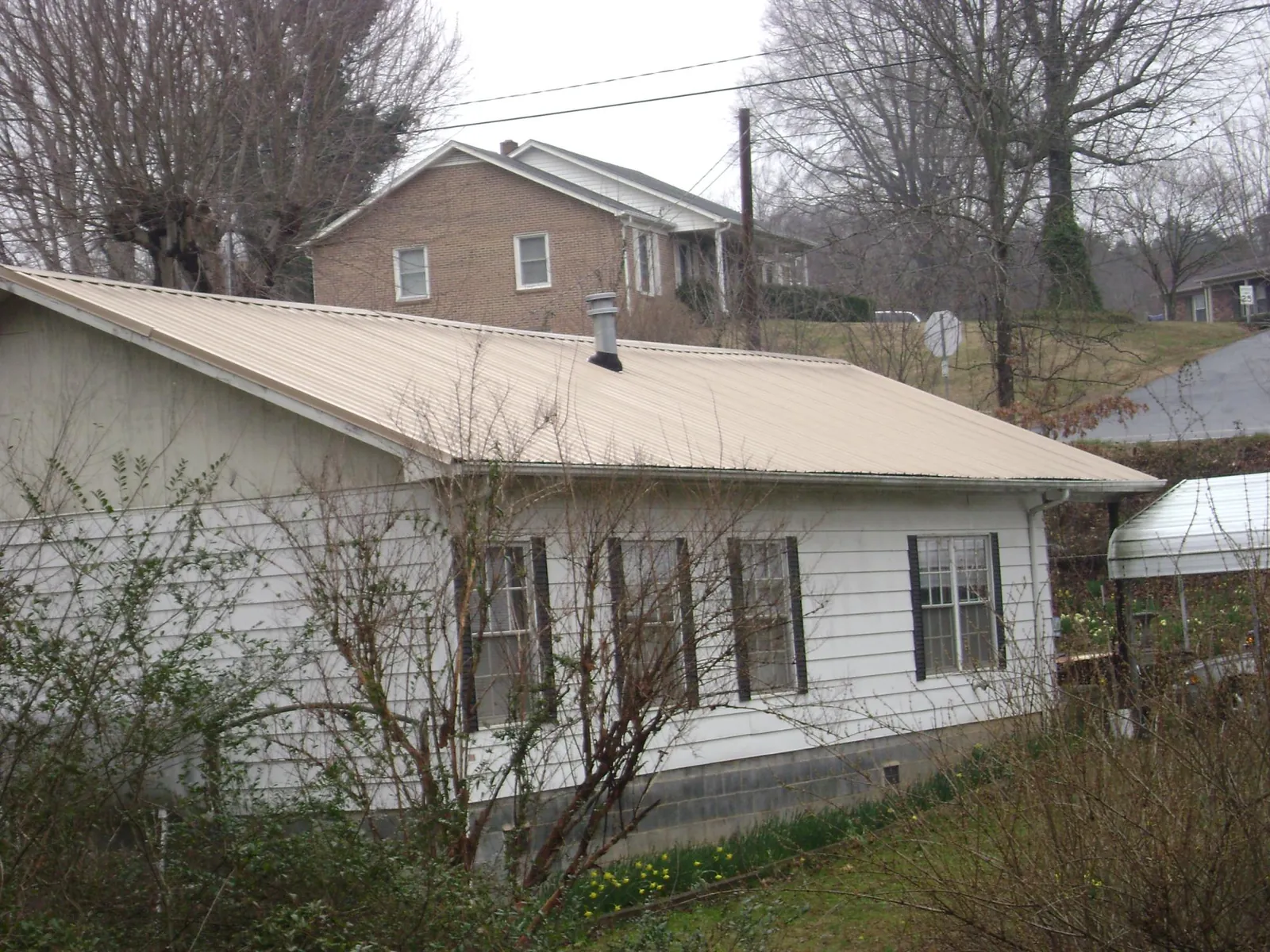 Tan metal roof on a white sided house set into a hillside — Commercial Roofing by Roofing Brothers in Plain Dealing