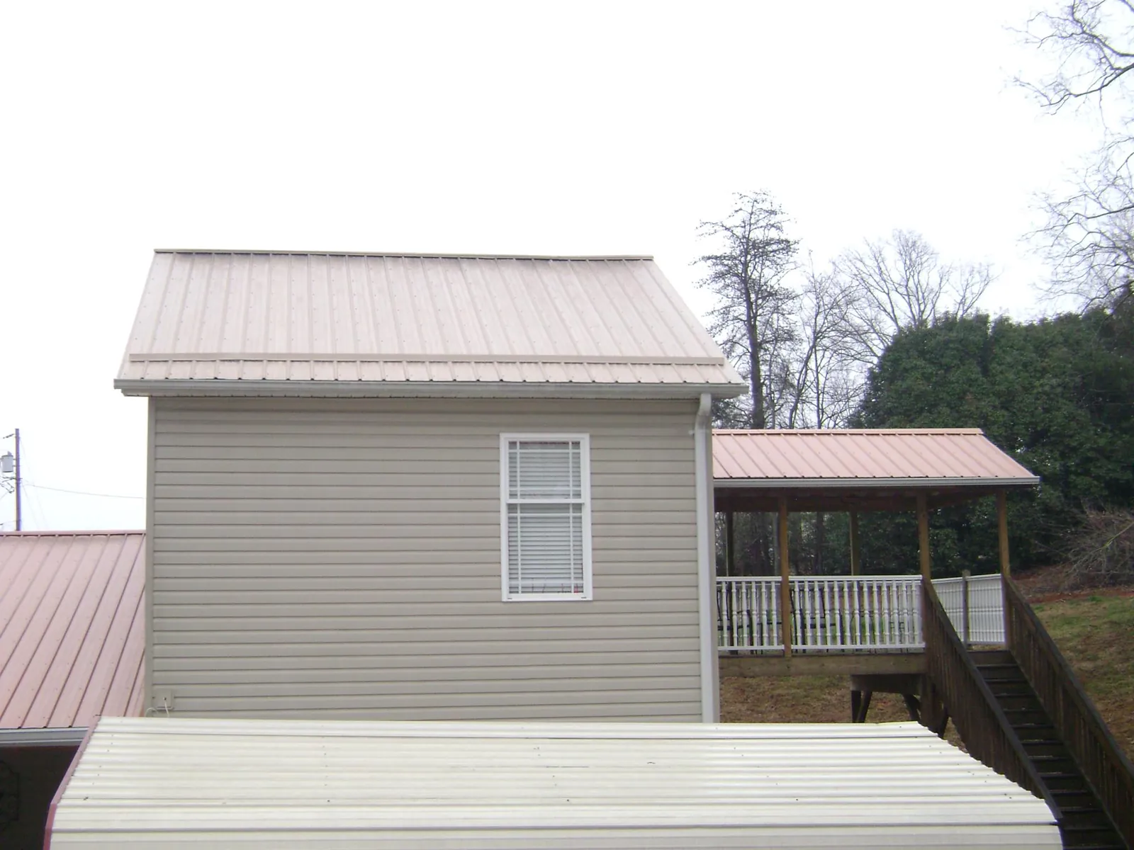 Tan metal roofs on a two story addition and attached porch, from a Roof Replacement job in Plain Dealing